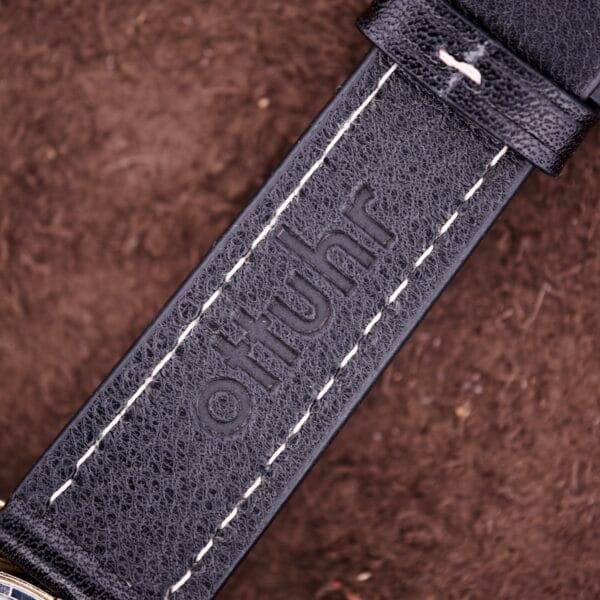 Close-up of a black leather strap with white stitching and "ottuhr" embossed, designed to complement the Bulova Accutron Turning Fork Cal. 2182 Day-Date Cushion Case or similar timepieces.