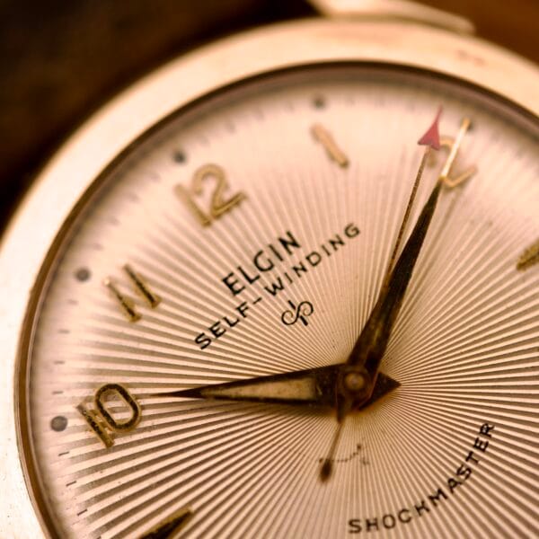 Close-up of an Elgin Automatic Shock-Master Guilloché Dial Cal. 643 watch face with gold numbers and hands, showing the time at about 1:10.