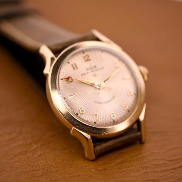 Close-up of the Elgin Automatic Shock-Master Guilloché Dial Cal. 643 wristwatch with a brown leather strap on a brown surface, showcasing its elegant guilloché dial.