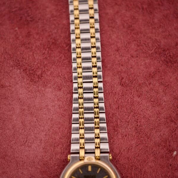 Close-up of a Gucci 9000 Ladies Watch with a black slate dial and two-tone gold and silver band, displayed on a textured maroon surface.