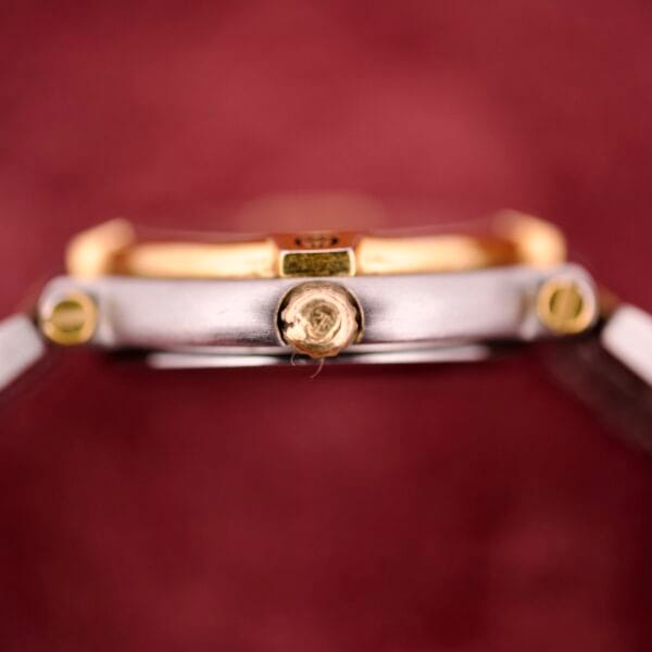 Close-up of the crown on a Gucci 9000 Ladies Watch Black Slate Dial Two-Tone Quartz, set against a blurred maroon background.