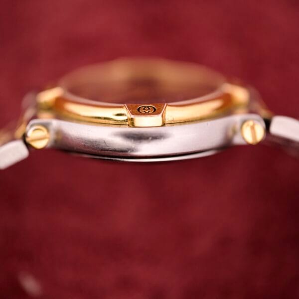 Side view of the Gucci 9000 Ladies Watch with a black slate dial and two-tone quartz finish, set against a blurred burgundy background.