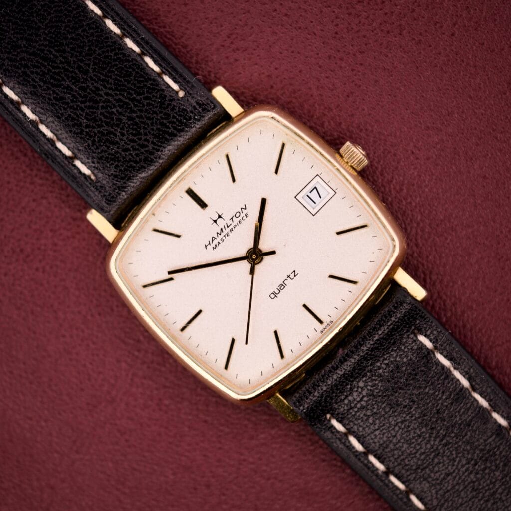 The Hamilton Masterpiece Ref. 9116 features a 10K gold-filled TV case, white dial, black leather strap, quartz movement, and date display set to 17.