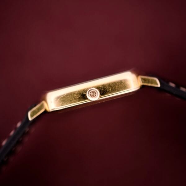 Close-up side view of a Hamilton Masterpiece Ref. 9116 10K Gold Filled TV Case Quartz wristwatch with a black strap, set against a dark red background.