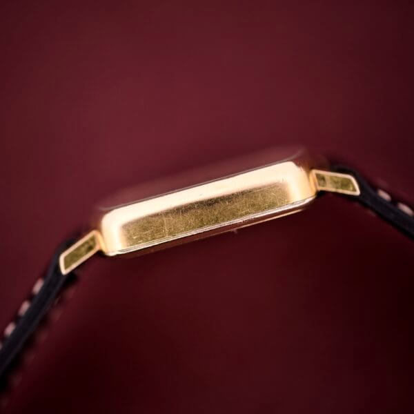 Side view of the Hamilton Masterpiece Ref. 9116, featuring a 10K gold filled TV Case Quartz and black straps, set against a dark red background.