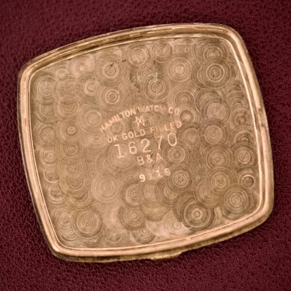 The Hamilton Masterpiece Ref. 9116 10K Gold Filled TV Case Quartz, engraved with Hamilton Watch Co and B&A (16270), rests elegantly on a burgundy surface.