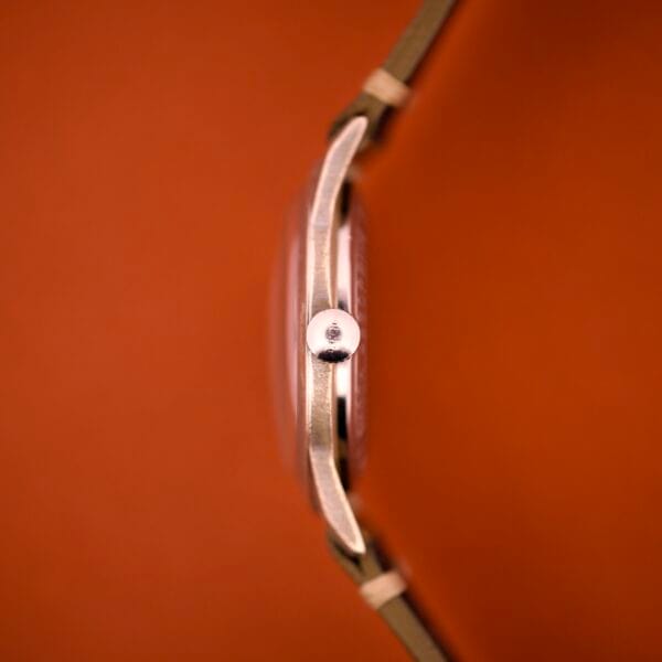 Side view of the Benrus Shock-Absorber Tropic Dial Silver Indices wristwatch with a round crown, displayed against an orange background.