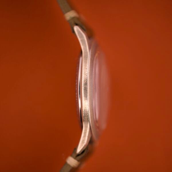 Side view of the Benrus Shock-Absorber Tropic Dial Silver Indices wristwatch with a metallic case and brown strap, displayed against an orange background.