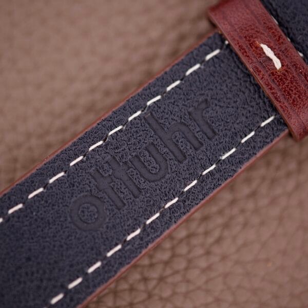 Close-up of a dark leather strap with white stitching and 'otiuhr' embossed, perfect for pairing with your Benrus Three Star Automatic Day-Date Sunburst Dial #7001 Series watch.
