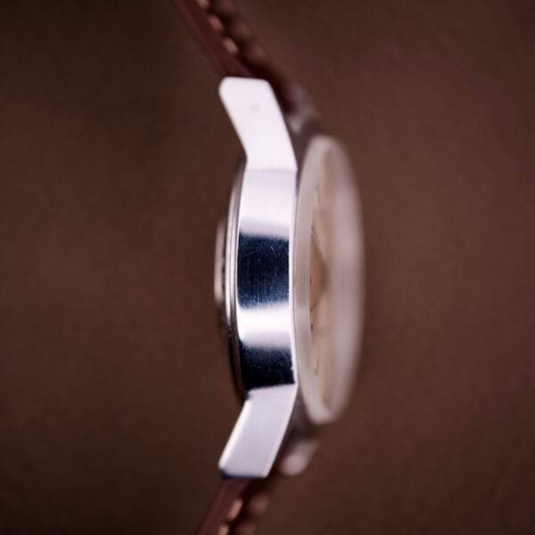 Close-up side view of the Benrus Three Star Automatic Day-Date Sunburst Dial #7001 Series with a brown leather strap and silver case, set against a brown background.