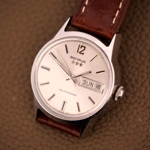 A Benrus Three Star Automatic Day-Date #7001 Series wristwatch with a sunburst dial, brown leather strap, and automatic day-date display set to Sunday the 16th.