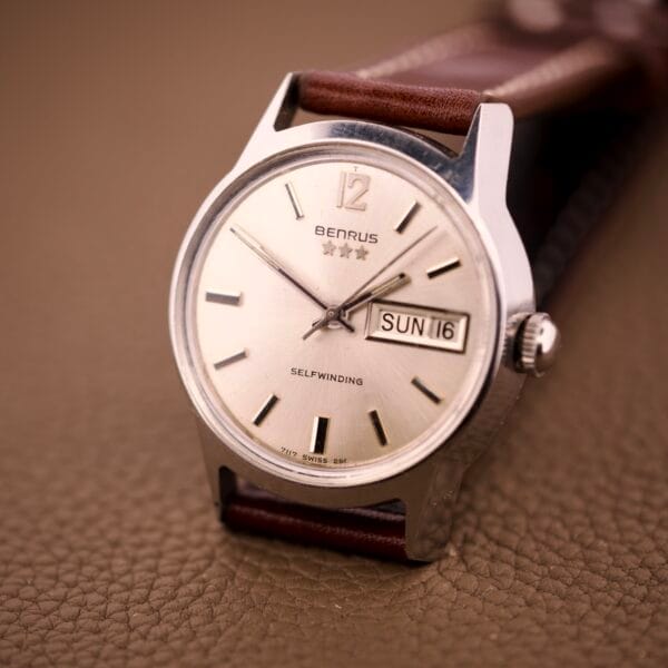 Close-up of a Benrus Three Star Automatic Day-Date Sunburst Dial #7001 Series wristwatch, featuring a sunburst dial, leather strap, and automatic day-date showing Sunday the 16th.