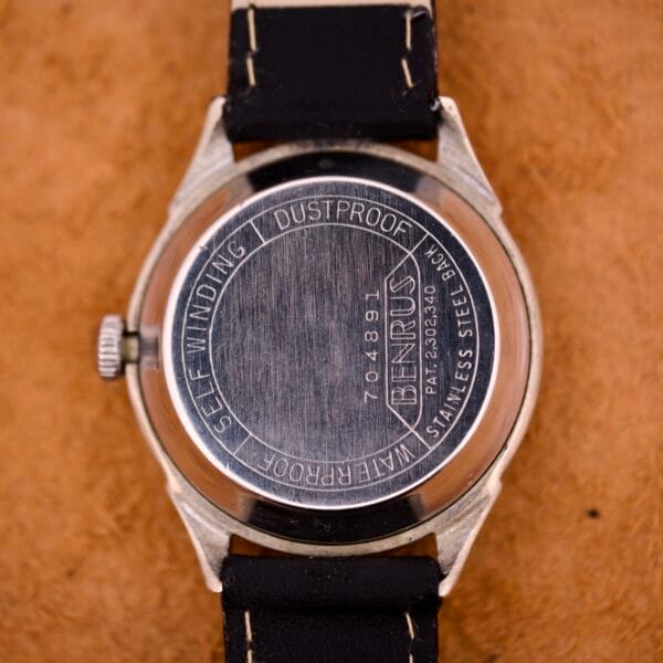 Back of a Benrus Three Star Automatic Browned Tropic Dial Stainless Steel watch with black leather strap, shown on a brown textured surface.