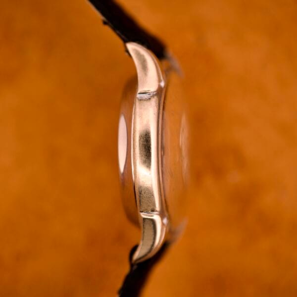 Side view of the Benrus Three Star Automatic Browned Tropic Dial Stainless Steel wristwatch with a leather strap, set against an orange-brown background.