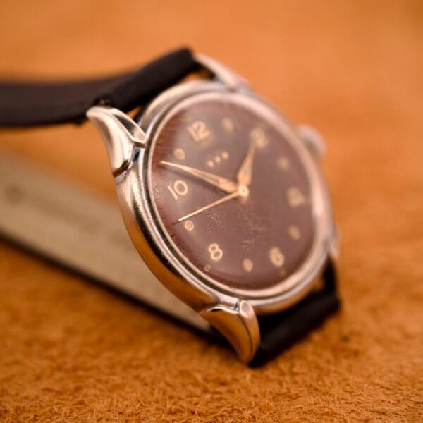 Close-up of a Benrus Three Star Automatic Browned Tropic Dial Stainless Steel wristwatch with a leather strap on a textured surface.
