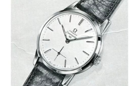 A silver Omega Seamaster 30 wristwatch with a white face and black leather strap rests on a light textured surface.