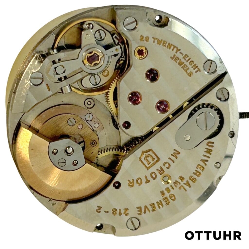 Close-up of a Universal Genève 218-9 watch movement showcasing intricate gears, jewels, and engraved text on its metallic surface.