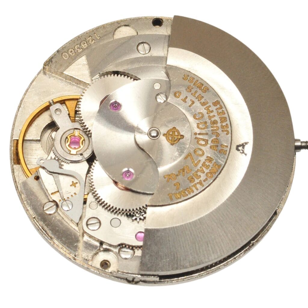 Close-up of a mechanical watch movement with gears, cogs, and engraved text on metal parts, featuring the 72B model designation.