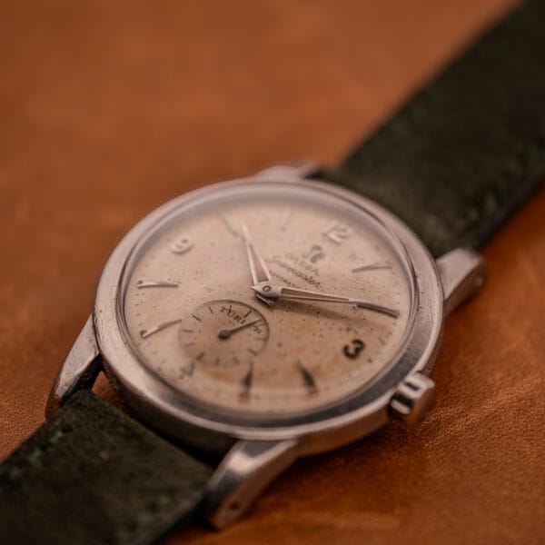 Dial-side angled view of Omega Seamaster showing tropical freckled patina across cream sub-seconds dial