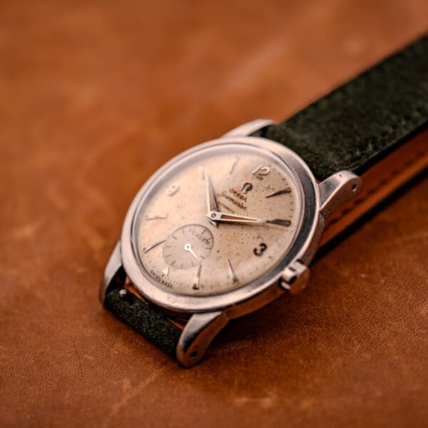 Omega Seamaster Bumper full case shot with olive suede strap and side-stitching on tan leather backdrop