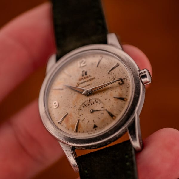 In-hand wrist view of Omega Seamaster Bumper Ref. 2576-14 showing dial scale against fingers and olive strap