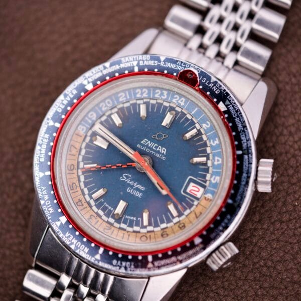 An Enicar Sherpa Guide 600 "Pepsi" Automatic World Timer GMT Ref. 2342, featuring a vibrant blue dial and metal bracelet, elegantly displayed on a brown surface.