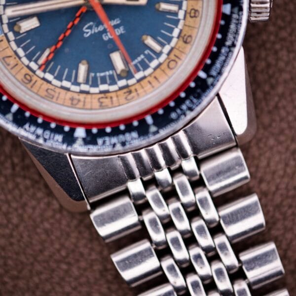 Close-up of an Enicar Sherpa Guide 600 "Pepsi" Automatic World Timer GMT Ref. 2342, featuring a stainless steel case and blue-beige dial, displayed on a textured brown surface.