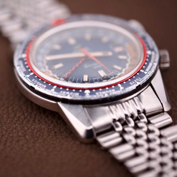 Close-up of an Enicar Sherpa Guide 600 "Pepsi" Automatic World Timer GMT Ref. 2342 with silver case, blue and red bezel, and metal link band on a brown surface.