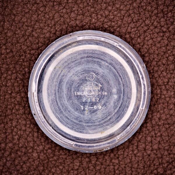 The engraved round metal case back of the Enicar Sherpa Guide 600 "Pepsi" Automatic World Timer GMT Ref. 2342 is displayed on a textured brown surface.