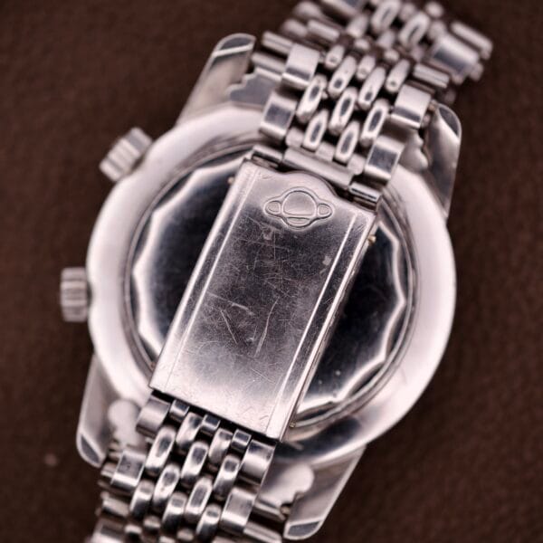 Close-up of an Enicar Sherpa Guide 600 "Pepsi" Automatic World Timer GMT Ref. 2342's silver clasp and band, showing scratches and the engraved logo.