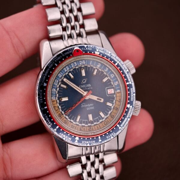 A hand holds the Enicar Sherpa Guide 600 "Pepsi" Automatic World Timer GMT Ref. 2342, featuring a metal band and a striking, colorful bezel.