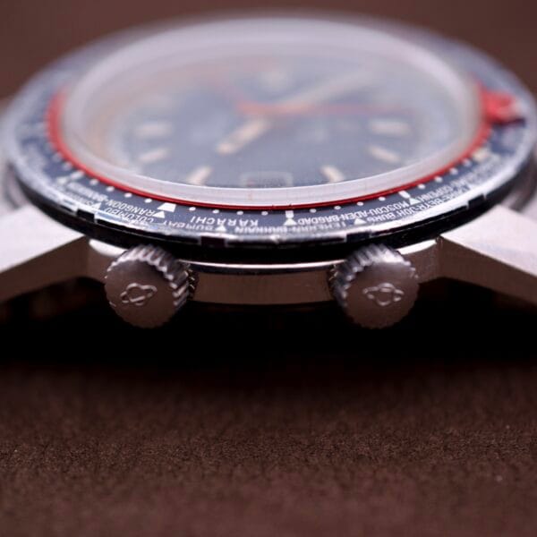 Close-up side view of the Enicar Sherpa Guide 600 "Pepsi" Automatic World Timer GMT Ref. 2342, highlighting its two crowns and part of the bezel, with the dial blurred in the background.