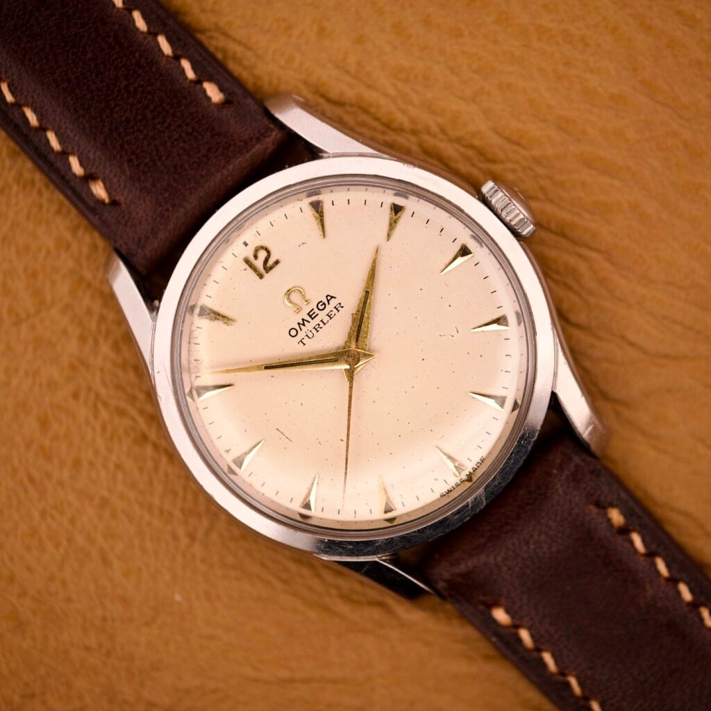 An Omega Jumbo Ref. 2640 Manual Wind Cal. 283 with a cream "Türler" dial and brown leather strap, displayed on a tan leather surface.