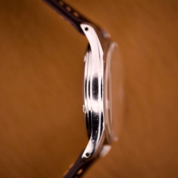 Side view of an Omega Jumbo Ref. 2640 Manual Wind Cal. 283 wristwatch with a silver case, brown leather strap, and "Türler" dial, shown against a blurred brown background.