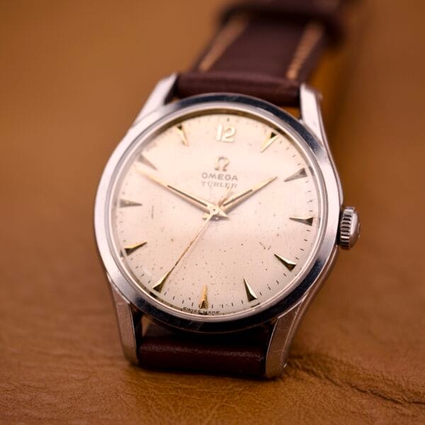 An Omega Jumbo Ref. 2640 Manual Wind Cal. 283 with a rare "Türler" Dial and brown leather strap is displayed elegantly on a tan surface.