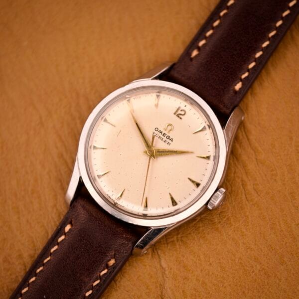 The Omega Jumbo Ref. 2640 Manual Wind Cal. 283 with a cream "Türler" dial and brown leather strap is elegantly displayed on a tan leather surface.
