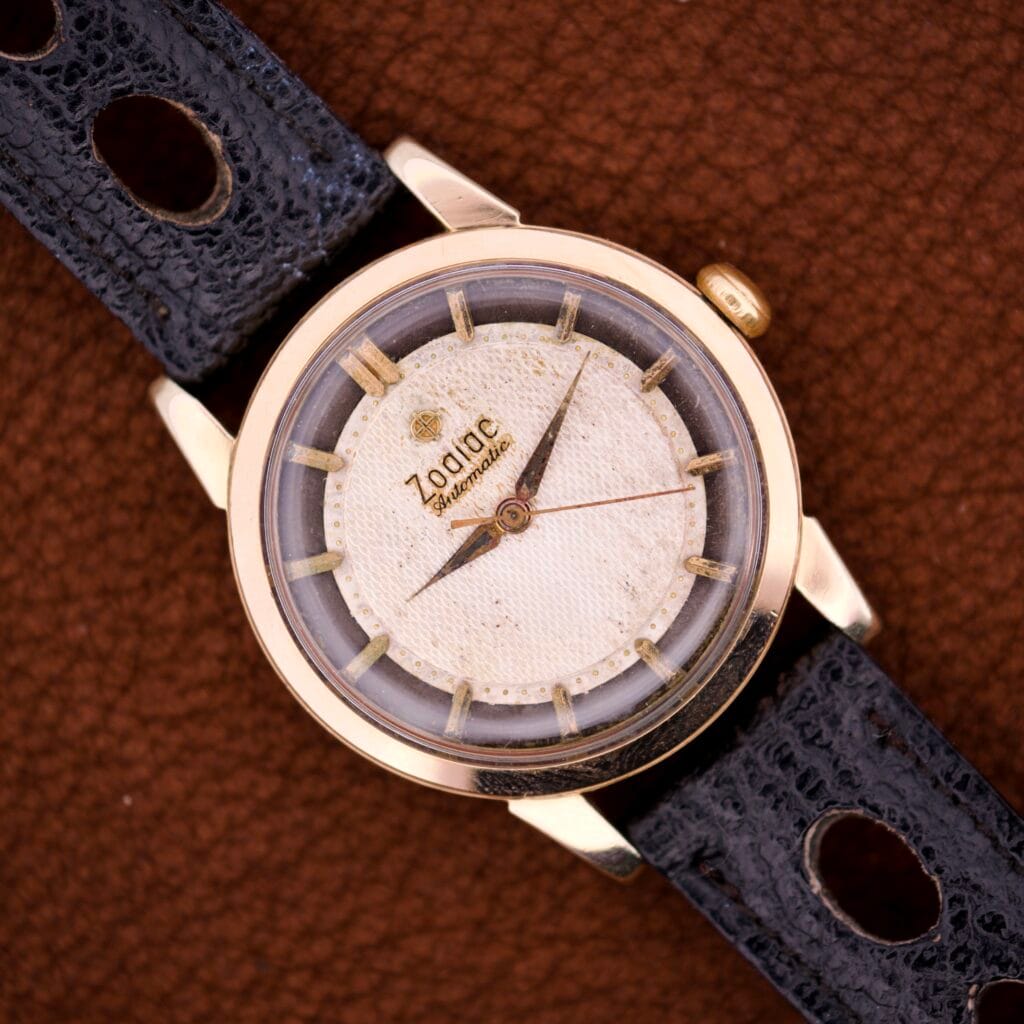 The Zodiac Glorious Automatic Tuxedo Dial Ref. 688 Cal. 1361 features a white dial and black leather strap, elegantly showcased on a brown textured surface.