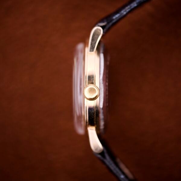 Side view of the Zodiac Glorious Automatic Tuxedo Dial Ref. 688 Cal. 1361 gold wristwatch with a black leather strap, set against a brown background.