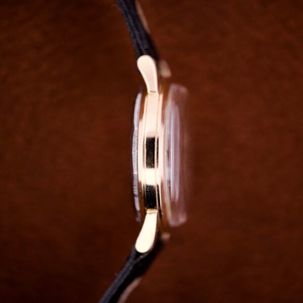 Side view of the Zodiac Glorious Automatic Tuxedo Dial Ref. 688 Cal. 1361 wristwatch with a black strap, highlighting its slim profile and tuxedo dial against a brown background.