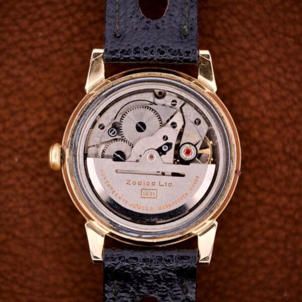 Close-up of a Zodiac Glorious Automatic Tuxedo Dial Ref. 688 (Cal. 1361) watch back, revealing exposed gears and inner mechanics on a brown background.