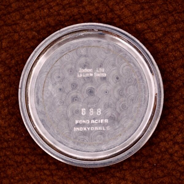 The case back of the Zodiac Glorious Automatic Tuxedo Dial Ref. 688 Cal. 1361, featuring engraved text, is shown resting on a brown textured surface.