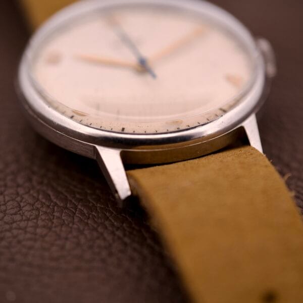Close-up of an Omega Ref. 2338 Jumbo with a stainless steel case, tan leather strap, and Caliber 30T2 SC movement, shown on a brown textured surface.