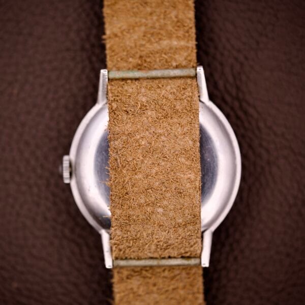 A close-up of an Omega Ref. 2338 Jumbo Caliber 30T2 SC with a brown suede strap and stainless steel case, showing the back of the watch against a dark surface.