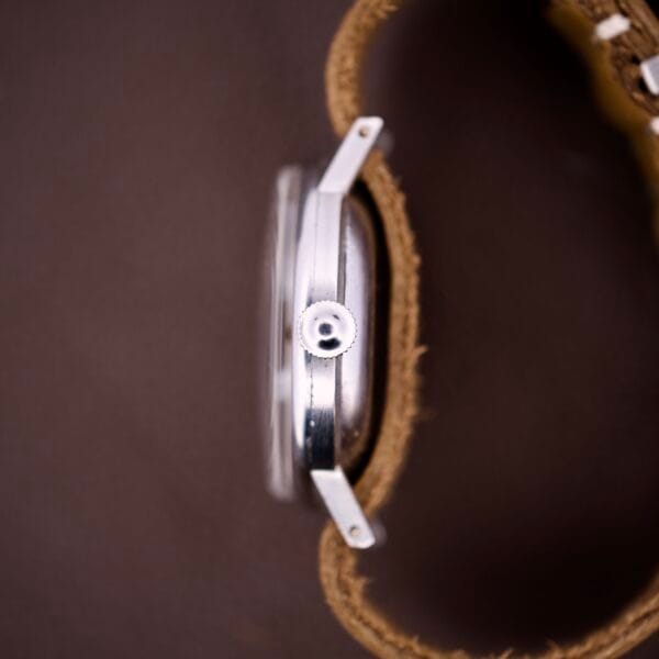 A close-up side view of the Omega Ref. 2338 Jumbo wristwatch with a brown leather strap and stainless steel case (Caliber 30T2 SC), resting on a brown surface.