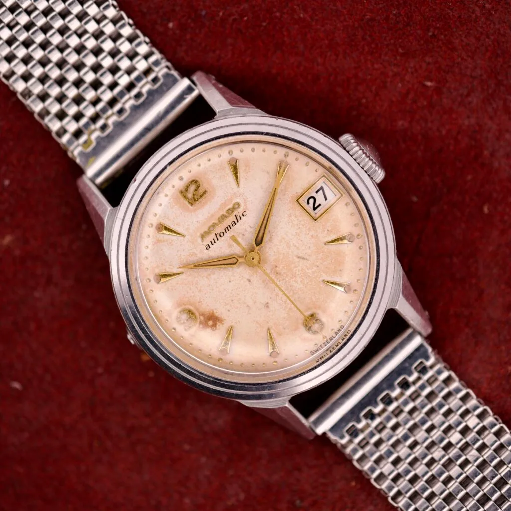 A vintage Movado Automatic Date Ref. 16291 wristwatch featuring a stainless steel mesh band and beige dial, with date 27 shown on a red background; powered by Bumper Cal. 224A movement.