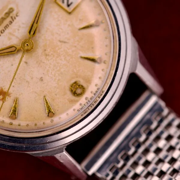 Close-up of a vintage Movado Automatic Date Ref. 16291 wristwatch with worn dial, stainless steel mesh band, “SWISS” text near the number six, featuring Bumper Cal. 224A movement.