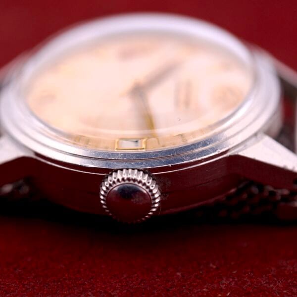 Close-up of a vintage Movado Automatic Date Ref. 16291 with a stainless steel crown and Bumper Cal. 224A, displayed on a red textured surface.