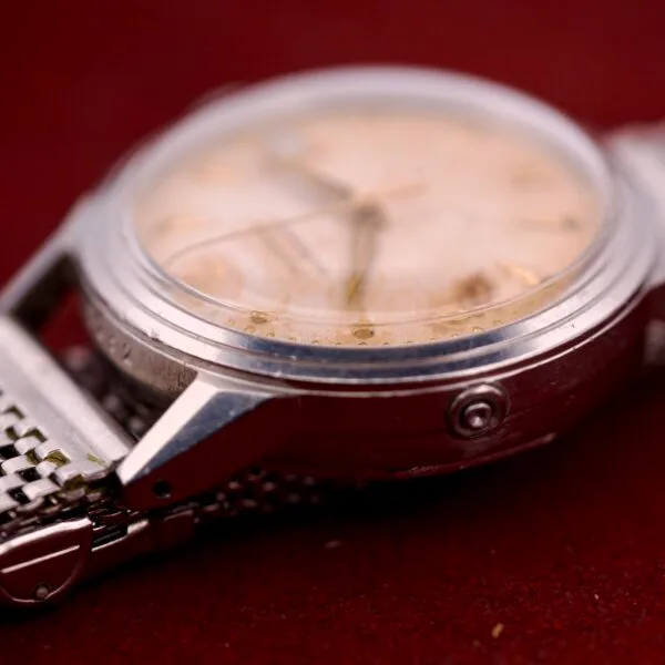 Close-up of a vintage Movado Automatic Date Ref. 16291 wristwatch with Bumper Cal. 224A, tarnished face, and stainless steel band, displayed on a red surface.