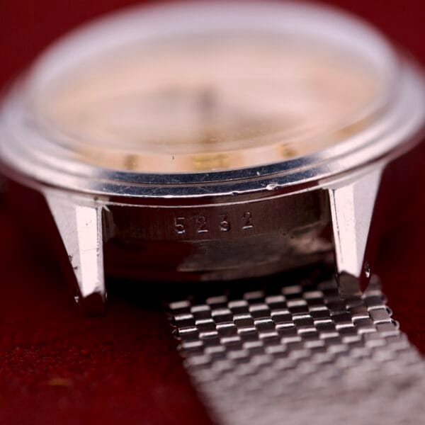 Close-up of a Movado Automatic Date Ref. 16291 stainless steel case with "5232" engraved between the lugs, shown on a metal mesh band.