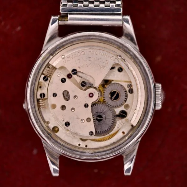 The internal mechanism of the Movado Automatic Date Ref. 16291 Stainless Steel Bumper Cal. 224A wristwatch, showcasing its distinctive gears and components, set against a red background.